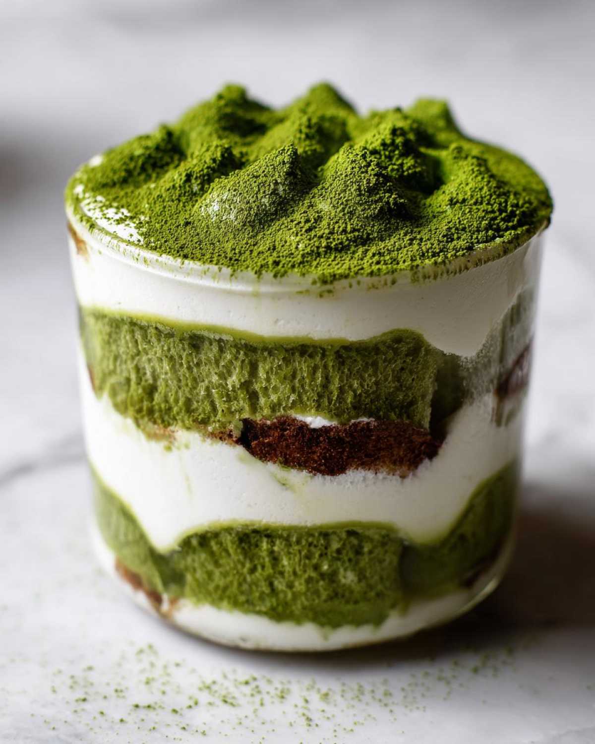 A single serving of Matcha Tiramisu Cups layered with green cake, cream, and heavily dusted with matcha powder.