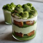 Close-up of a layered Matcha Tiramisu Cups dessert in a glass, showing ladyfingers, green cream, and heavy matcha powder dusting.