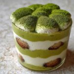 Close-up of a layered Matcha Tiramisu Cups dessert in a glass, dusted heavily with green matcha powder.