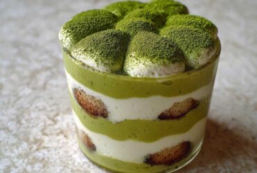 Close-up of a layered Matcha Tiramisu Cups dessert in a glass, dusted heavily with green matcha powder.
