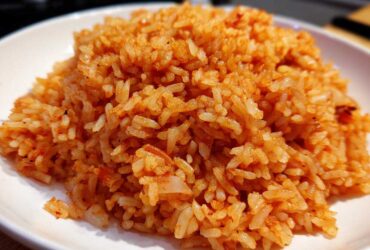 Close-up of perfectly cooked Mexican Rice with Roasted Garlic, showing individual orange-red grains piled on a white plate.
