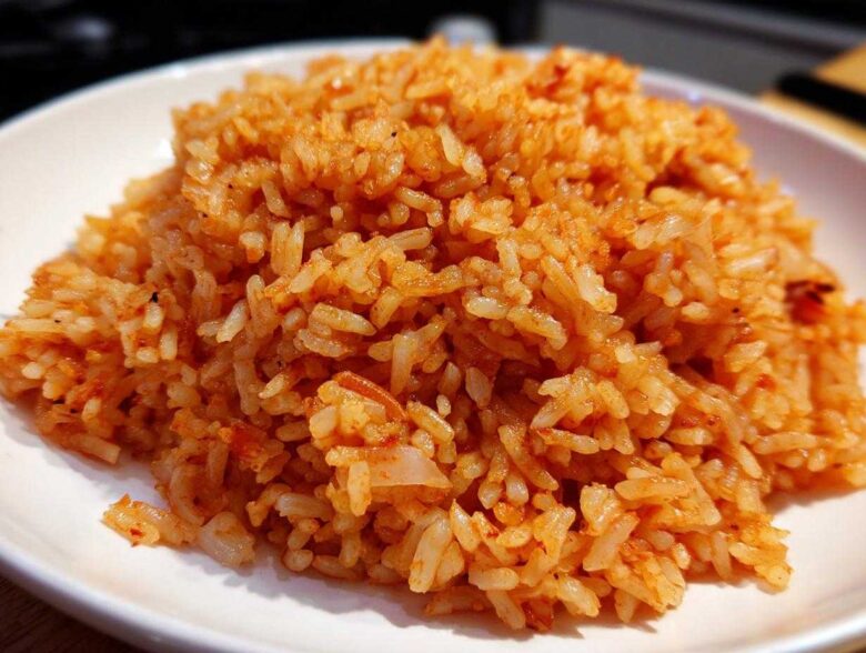 Close-up of perfectly cooked Mexican Rice with Roasted Garlic, showing individual orange-red grains piled on a white plate.