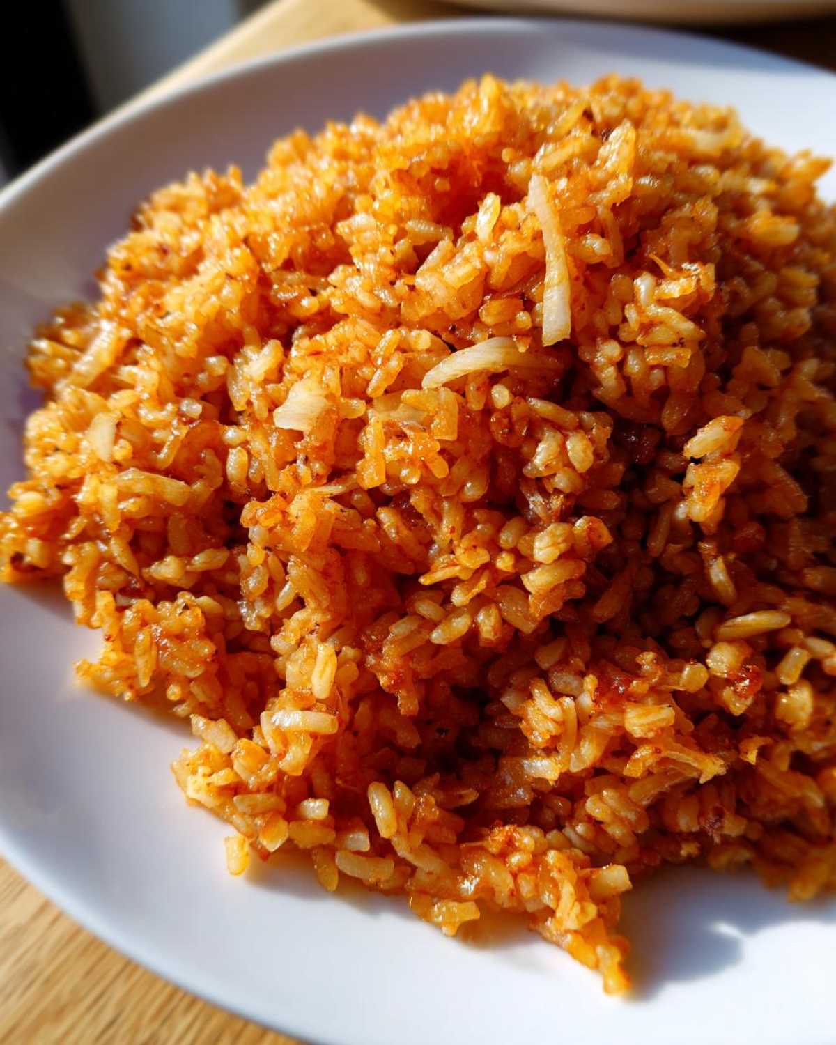Close-up of a mound of vibrant orange Mexican Rice with Roasted Garlic piled high on a white plate.