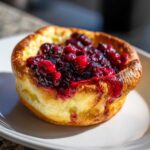A single, golden-brown Mini Dutch Baby Pancakes topped generously with rich, dark berry compote.