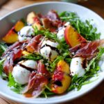 Close-up of a refreshing Peach Burrata Prosciutto Salad featuring fresh arugula, mozzarella balls, and a dark balsamic drizzle.