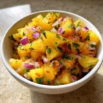 Close-up of vibrant Pineapple Habanero Salsa with chunks of pineapple, red onion, and cilantro in a white bowl.