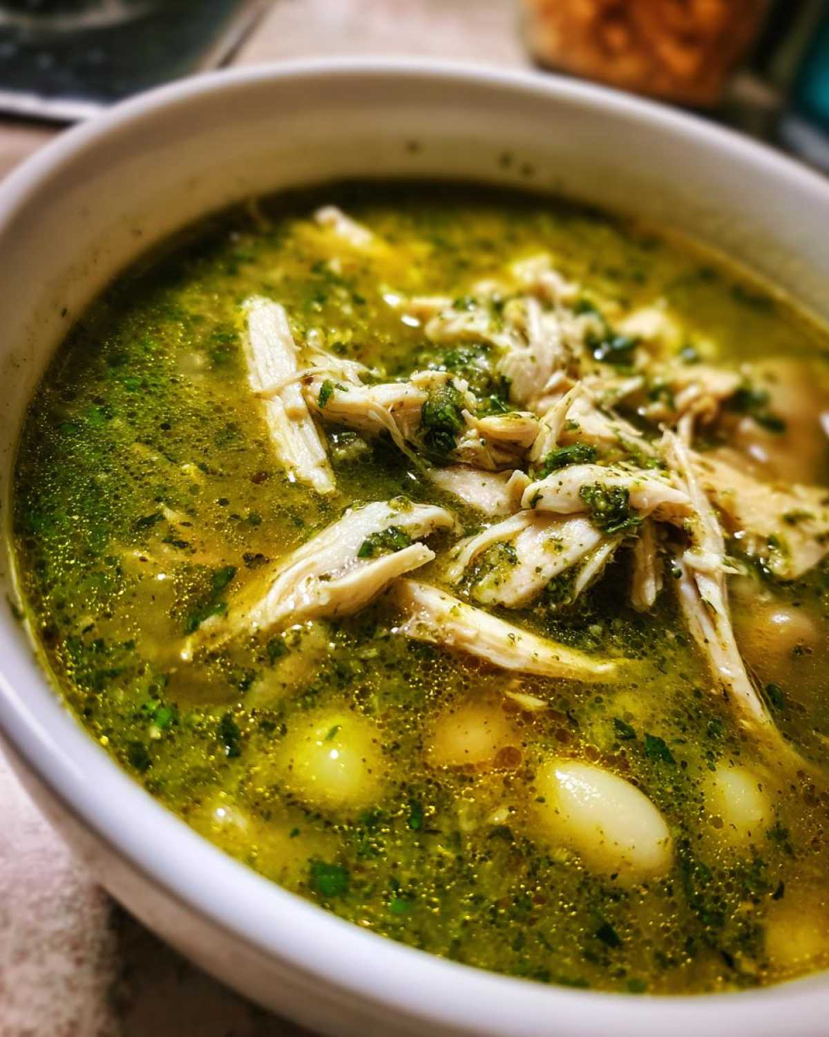 A close-up view of a white bowl filled with vibrant green Pozole Verde Chicken Soup, showing shredded chicken and hominy.