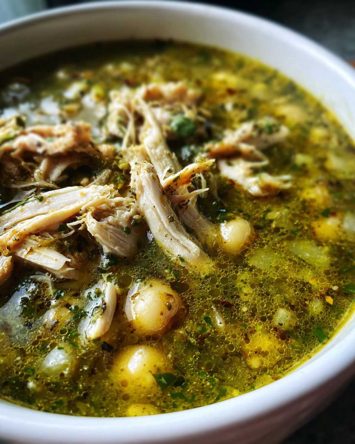 Close-up shot of shredded chicken and hominy in a vibrant green broth of Pozole Verde Chicken Soup.