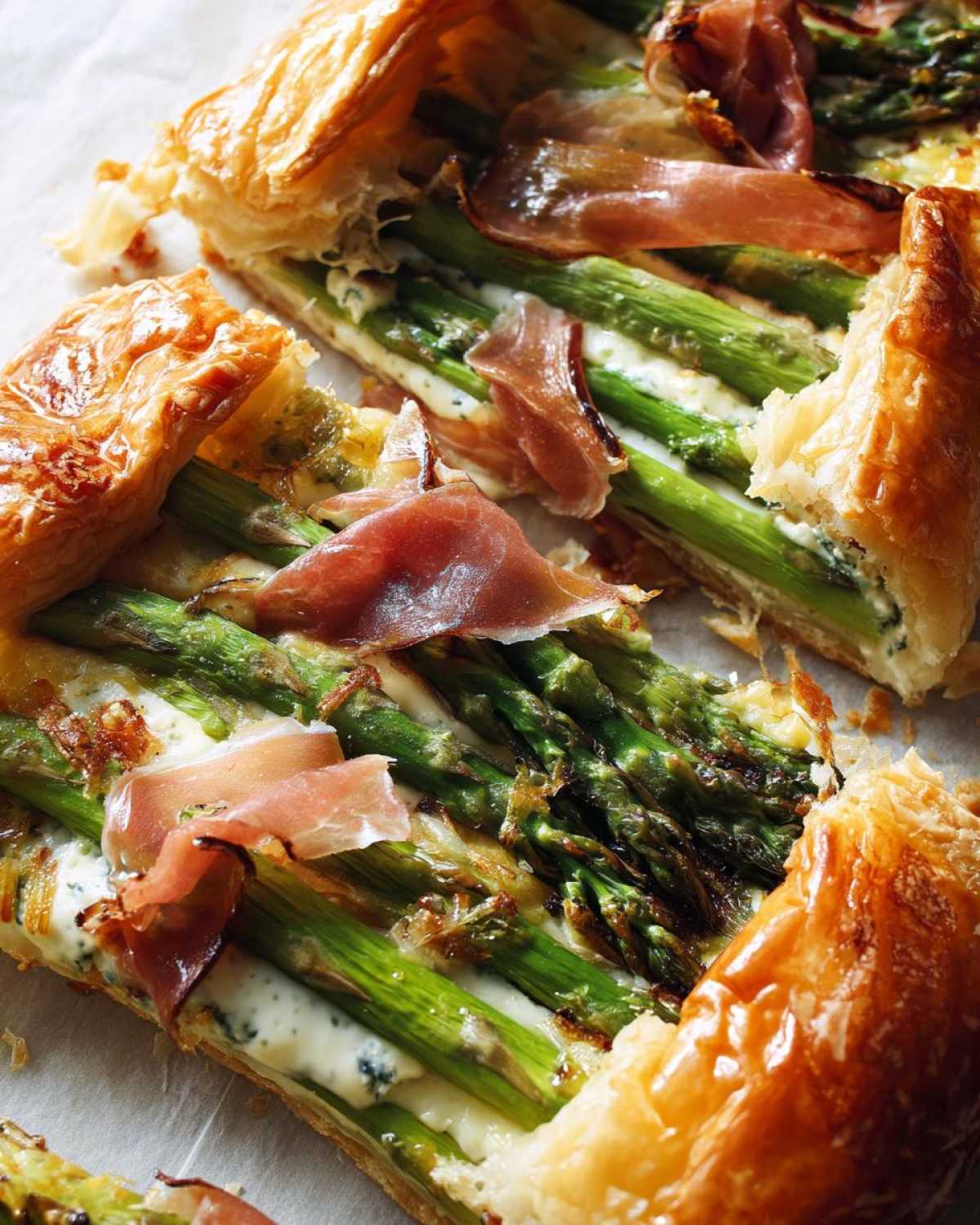 Close-up of slices of Prosciutto Asparagus Tart showing flaky golden crust, bright green asparagus, and draped prosciutto.