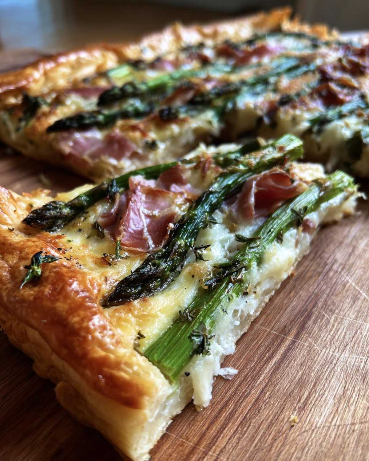 Close-up of a slice of Prosciutto Asparagus Tart showing flaky crust, green asparagus spears, and prosciutto.
