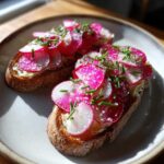 Two slices of Radish Butter Tartines with Flaky Salt, topped with bright pink radishes and chives on toasted bread.