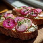 Two slices of toasted bread topped with butter, vibrant pink and white radish slices, chives, and flaky salt, ready for Radish Butter Tartines.