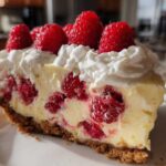 A close-up slice of Raspberry Lemonade Icebox Pie showing the creamy filling, whole raspberries, graham cracker crust, and whipped cream topping.