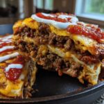 A thick, layered slice lifted from the Refried Bean Crunchwrap Skillet, showing seasoned meat, cheese, and topped with sour cream and salsa.