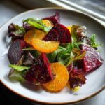 Close-up of a vibrant Roasted Beet Orange Salad featuring deep red beet wedges, bright orange citrus slices, and mixed leafy greens.
