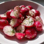 Close-up of bright pink Roasted Radishes with Garlic and Dill, halved and glistening in a white bowl.