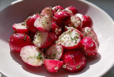 Close-up of bright pink Roasted Radishes with Garlic and Dill, halved and glistening in a white bowl.