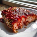A close-up of a perfectly cooked fillet of Sesame Strawberry-Glazed Salmon, topped with a thick red glaze and sesame seeds.