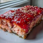 Close-up of a thick slice of cooked salmon topped with bright red strawberry glaze and sesame seeds, part of the Sesame Strawberry-Glazed Salmon recipe.