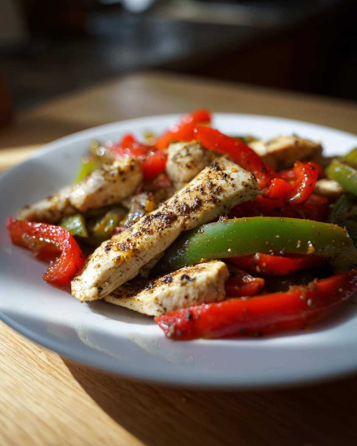 Close-up of seasoned chicken strips mixed with bright red and green bell peppers for Sheet-Pan Chicken Fajitas.