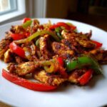 A close-up of seasoned chicken strips mixed with vibrant red and green bell peppers and onions, ready to serve as Sheet-Pan Chicken Fajitas.