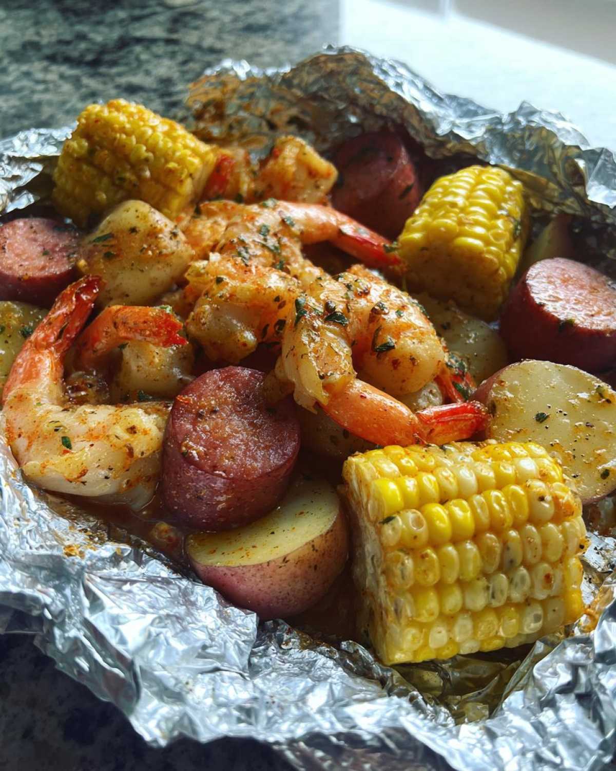 Close-up of cooked shrimp, smoked sausage, corn on the cob, and potatoes inside a foil packet for Shrimp Boil Foil Packets.