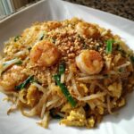 A close-up of delicious Pad Thai with Tamarind Sauce, topped with shrimp, crushed peanuts, and green onions.