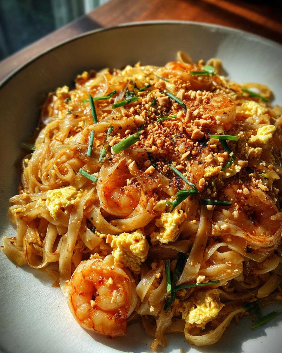 Close-up of vibrant shrimp Pad Thai with tamarind sauce, scrambled eggs, and crushed peanuts.