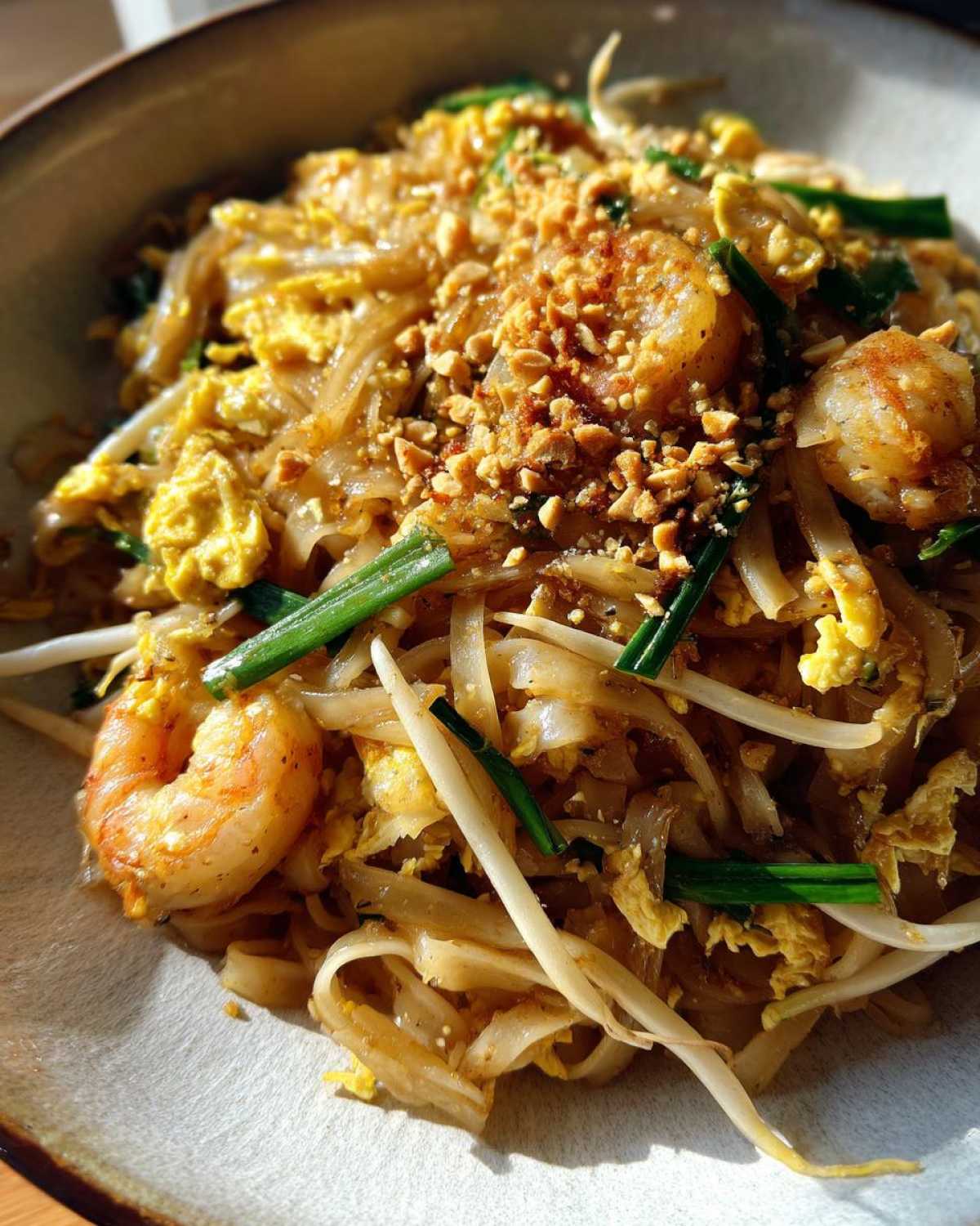 A close-up, overhead view of a bowl of delicious Pad Thai with Tamarind Sauce, featuring shrimp, scrambled egg, bean sprouts, and crushed peanuts.