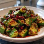 Close-up of vibrant green chunks in a Sichuan Smash Cucumber Salad, coated in spicy chili oil and sesame seeds.