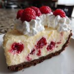 A close-up of a slice of Raspberry Lemonade Icebox Pie showing the creamy filling, whole raspberries, and whipped cream topping.