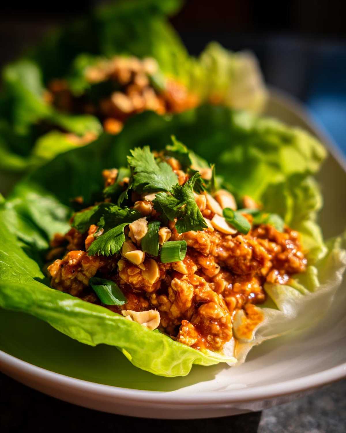Close-up of a Spicy Peanut Chicken Lettuce Cups serving topped with cilantro and chopped peanuts.