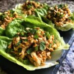 A close-up of one serving of Spicy Peanut Chicken Lettuce Cups, topped with chopped peanuts and green onions.