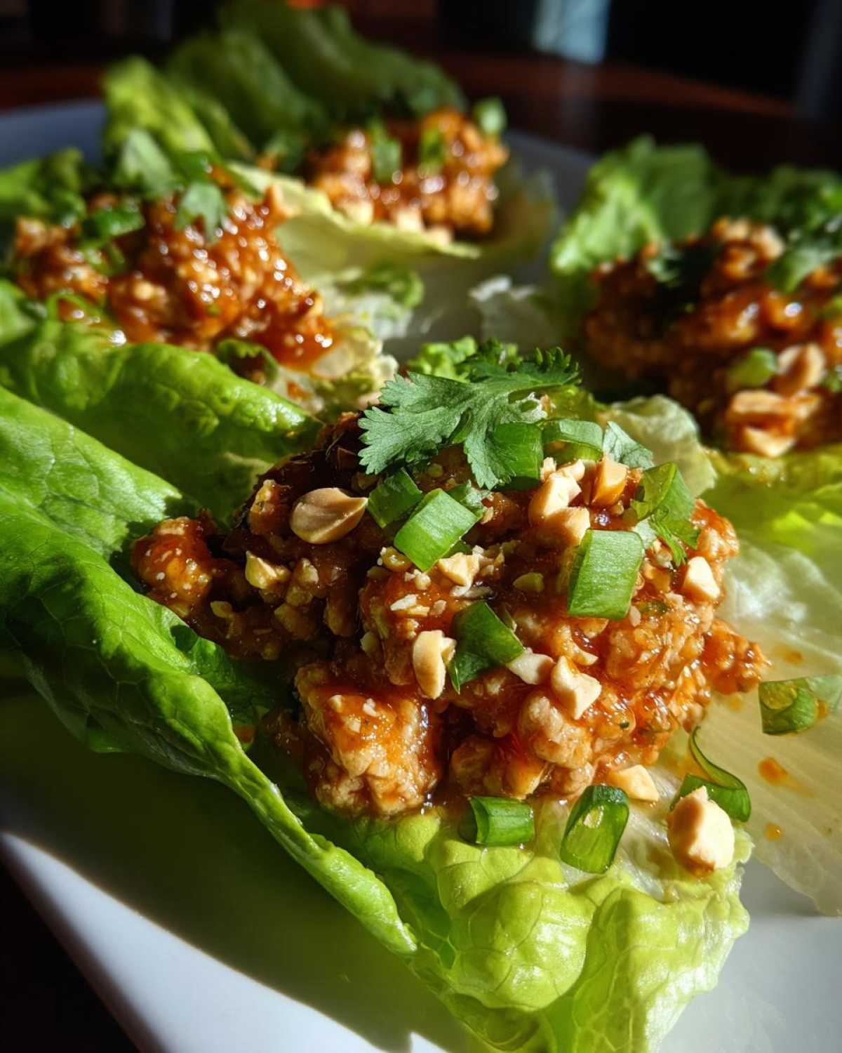 Close-up of a Spicy Peanut Chicken Lettuce Cups portion topped with chopped peanuts and green onions.