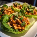 Close-up of three servings of Spicy Peanut Chicken Lettuce Cups garnished with chopped peanuts and cilantro.