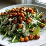 A vibrant Spring Greens Caesar with Crispy Chickpeas, drizzled with creamy dressing, served on a white plate.