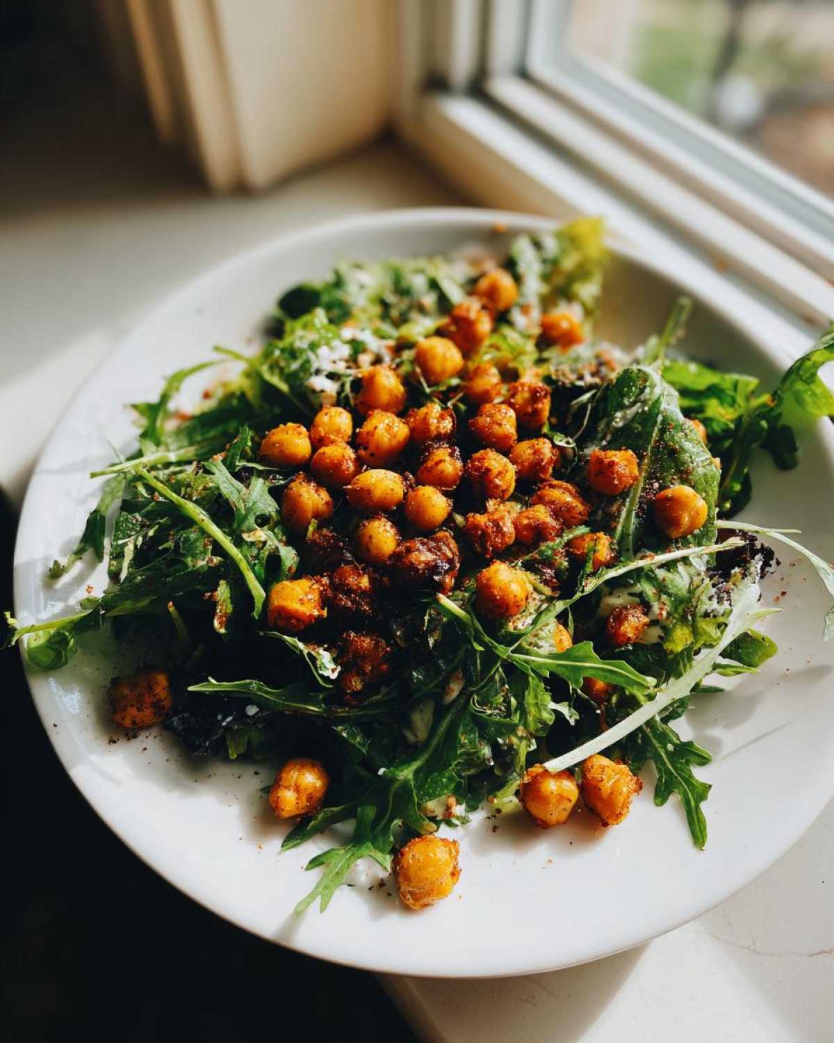 A vibrant plate of Spring Greens Caesar with Crispy Chickpeas, featuring dark leafy greens and seasoned roasted chickpeas.