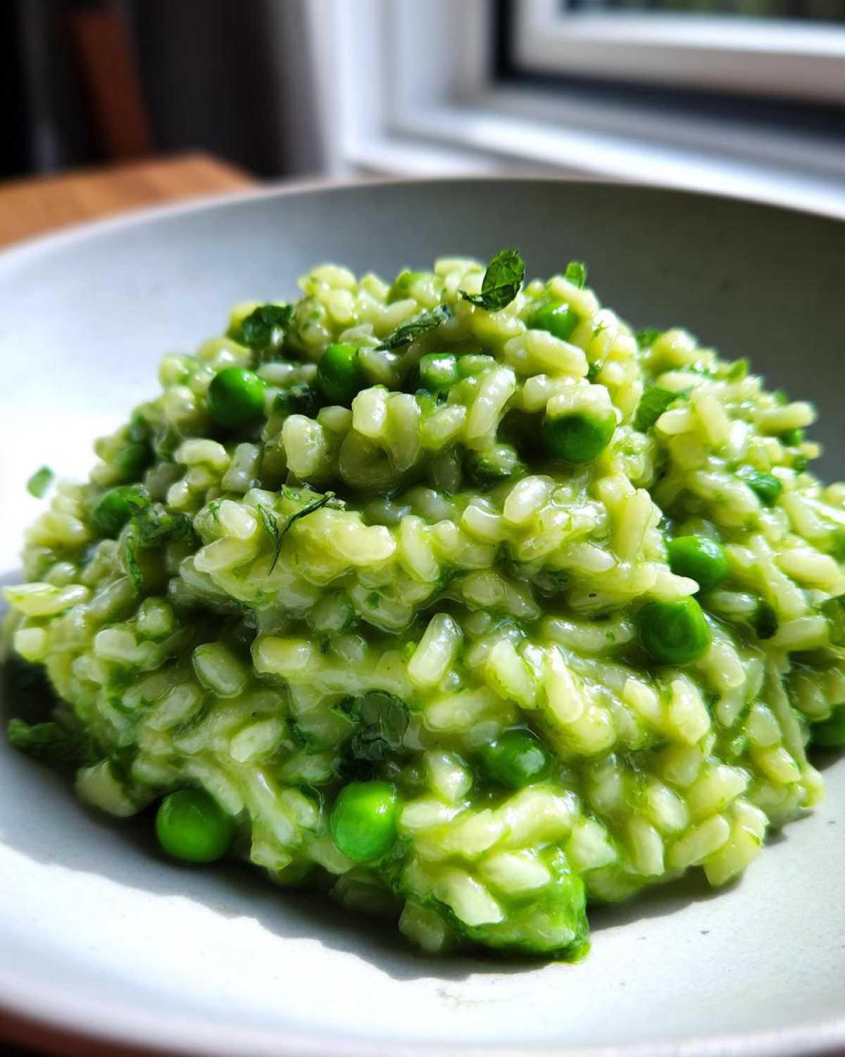 A close-up of creamy Spring Pea Mint Risotto, vibrant green with whole peas and fresh mint garnish.