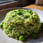 A molded serving of creamy Spring Pea Mint Risotto garnished with whole peas and fresh mint.