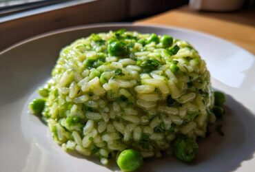 A molded serving of creamy Spring Pea Mint Risotto garnished with whole peas and fresh mint.