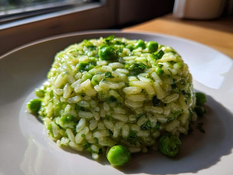 A molded serving of creamy Spring Pea Mint Risotto garnished with whole peas and fresh mint.