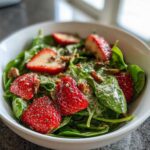 Close-up of a vibrant Spring Strawberry Spinach Salad featuring bright red strawberries, pecans, and creamy poppy seed dressing.
