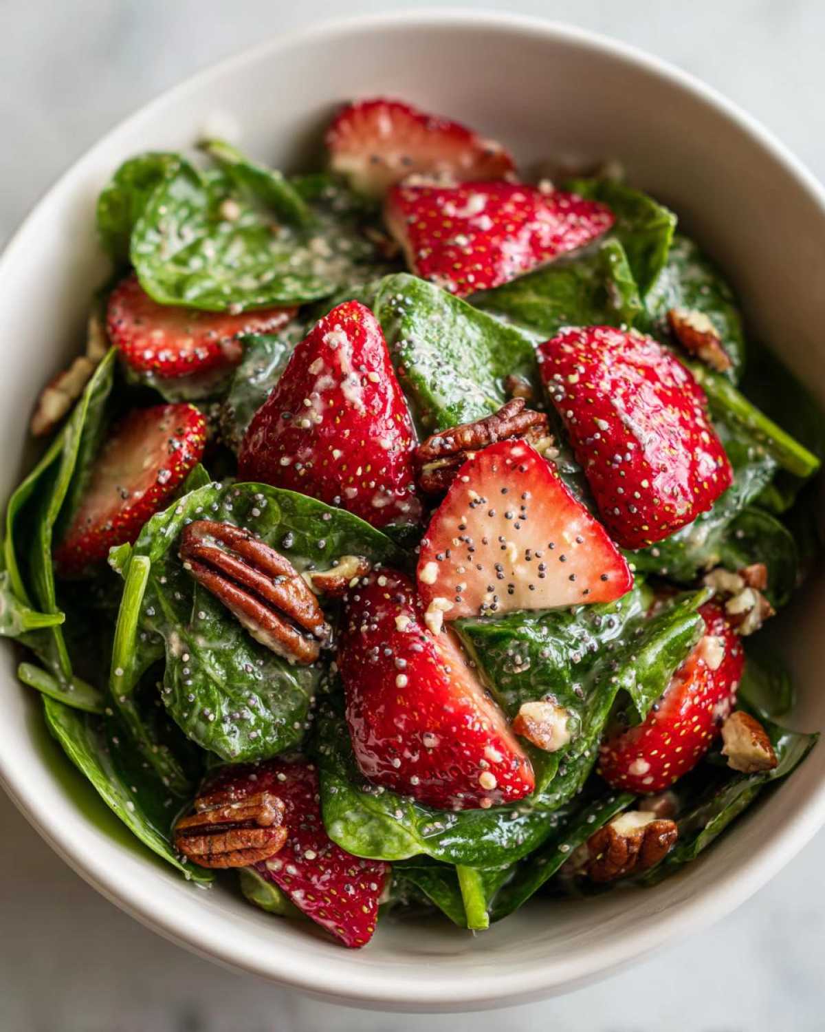 Close-up of a bowl filled with Spring Strawberry Spinach Salad, featuring fresh spinach, sliced strawberries, pecans, and poppy seed dressing.