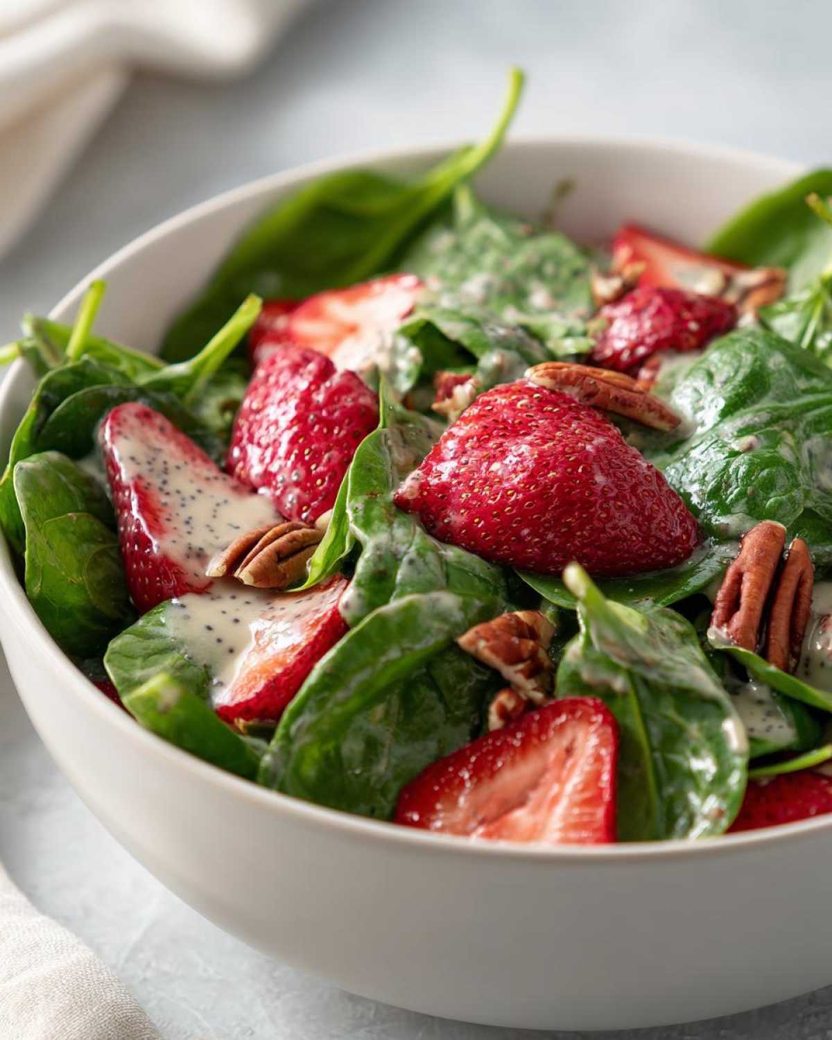 A close-up of a fresh Spring Strawberry Spinach Salad topped with pecans and creamy poppy seed dressing.