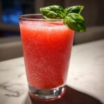 Close-up of a vibrant red Strawberry Basil Lemonade Slush garnished with fresh basil leaves.