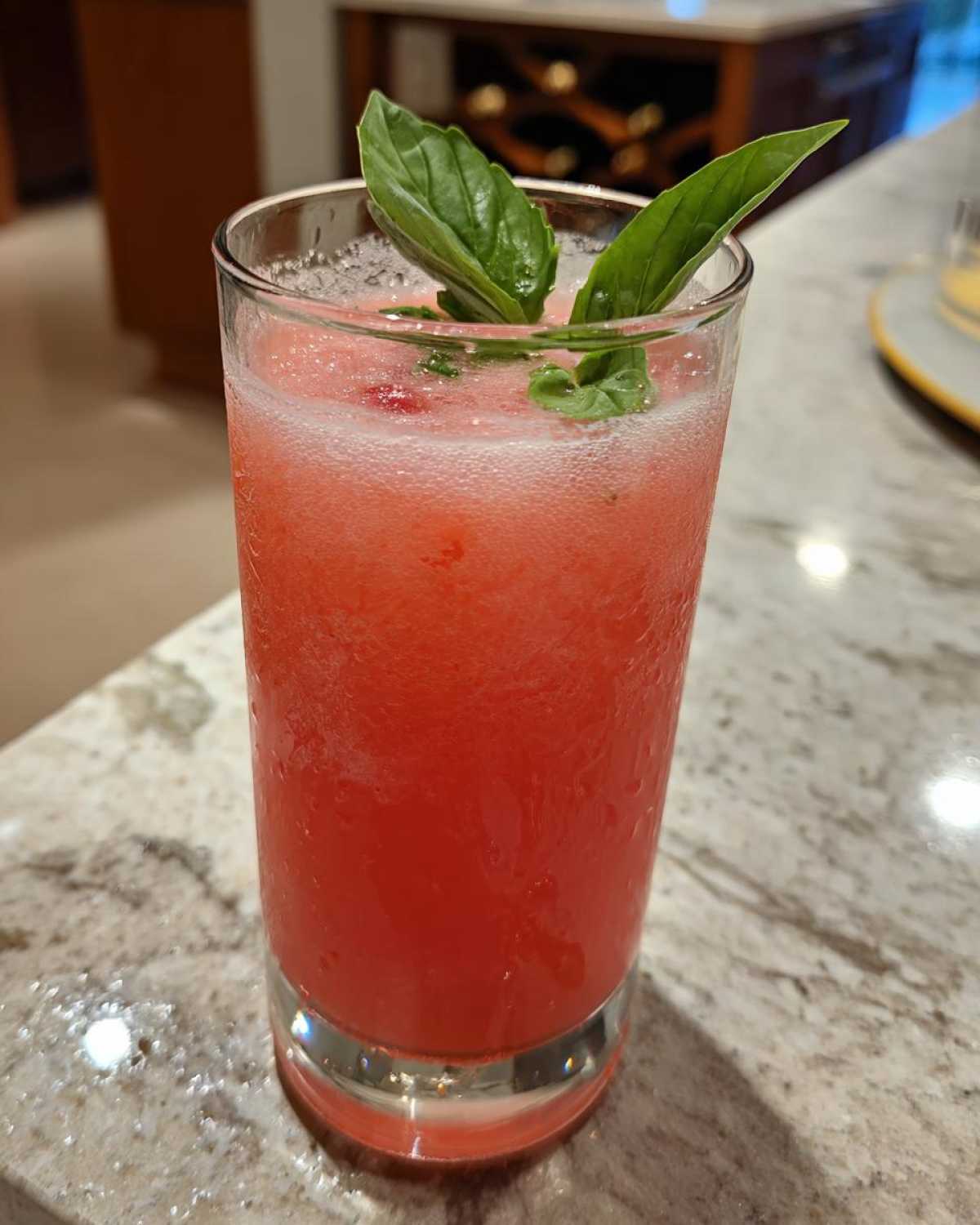 A tall glass filled with bright red Strawberry Basil Lemonade Slush, garnished with fresh basil leaves.