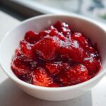 Close-up of bright red, chunky 10-Minute Strawberry Chia Jam served in a small white bowl.