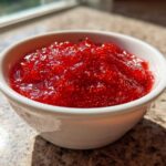 Close-up of bright red 10-Minute Strawberry Chia Jam texture in a small white bowl.