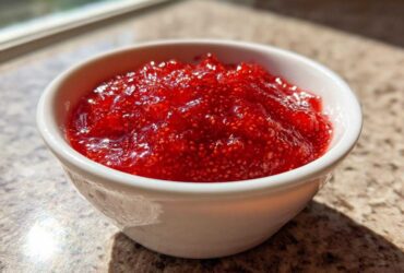 Close-up of bright red 10-Minute Strawberry Chia Jam texture in a small white bowl.