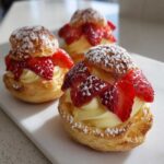 Three delicious Strawberry Cream Puff Tartlets filled with pastry cream and topped with sliced strawberries and powdered sugar.